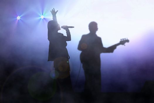 Women on stage singing with guitarist under spotlight