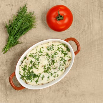 Julienne mushrooms baked in cream sauce, in a bowl for baking on a wooden background. Bunch of dill and tomato, place for text.