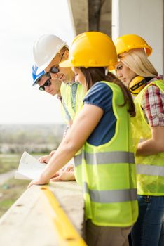 Four construction architects review plan at a construction site.