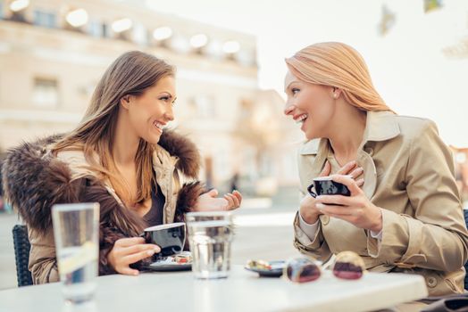 Young cheerful female friends sitting in a street cafe and enjoying coffee.