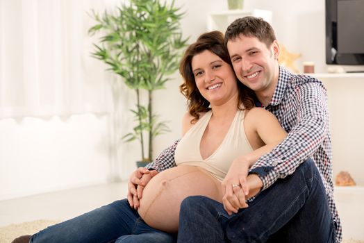 Portrait of a beautiful young couple cuddling the woman's pregnant belly. They smiling and looking at camera.