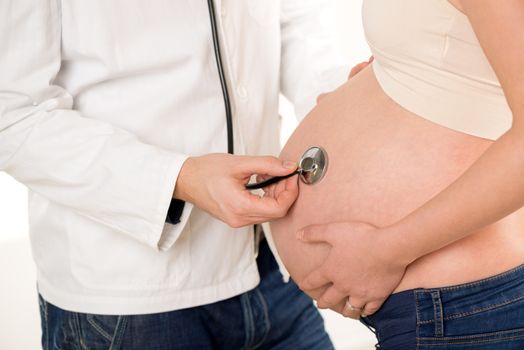 Pregnant woman examining by a doctor with a stethoscope. Close-up.