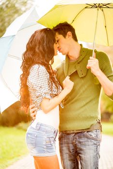 Young boy and girl standing embracing under umbrellas and they kiss.