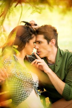 Young couple in love sitting on a park bench, illuminated by sunlight, passionate look at each other in the moment before the kiss.