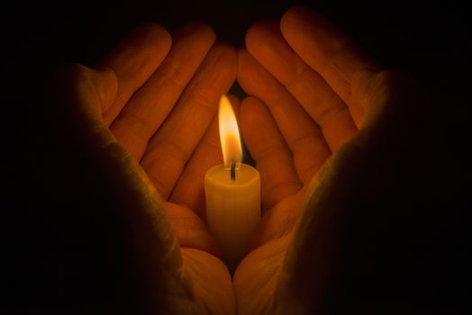 Protective hands around a burning candle
