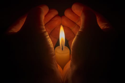 Protective hands around a burning candle
