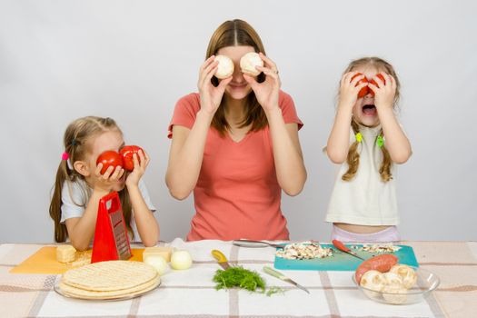 Mum with two little girls having fun at the kitchen table playing with vegetables