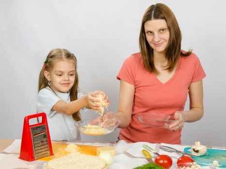  Six-year girl helps mother to rub grated cheese on pizza