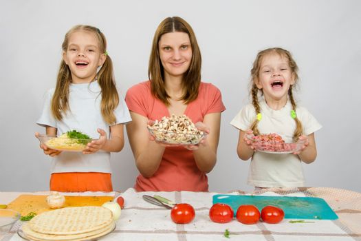 Mother with two daughters happily holding a plate with sliced products for pizza