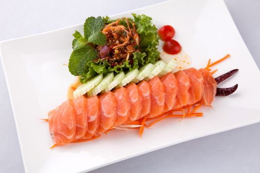 sashim salmon with spicy salad on a white plate