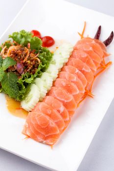 sashim salmon with spicy salad on a white plate