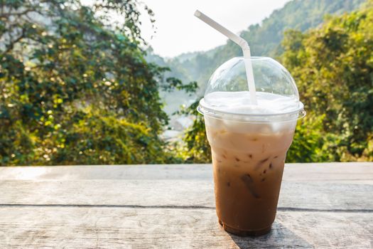 Iced coffee on wooden table with mountain view in background.