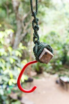 Red hook tied with nylon rope.Blurred tree in background.