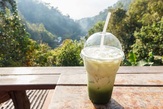 Green tea on wooden table with mountain view in background.