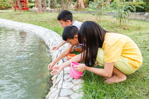 Young Thai children feeding fish in pond.