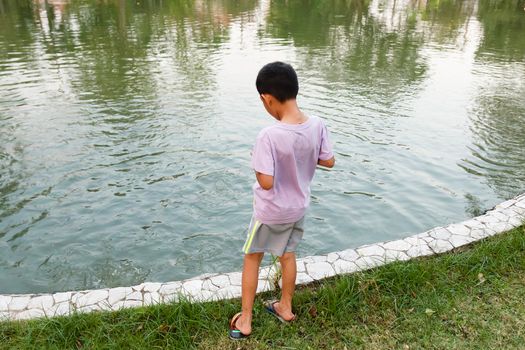 Young Thai boy feeding fish in pond.