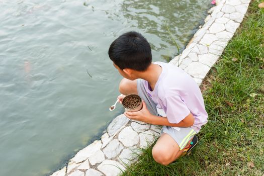 Young Thai boy feeding fish in pond.