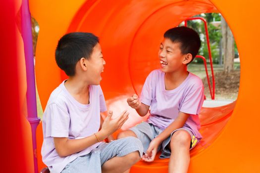 Twin Thai boy playing rock-paper-scissors and laughing at playground.