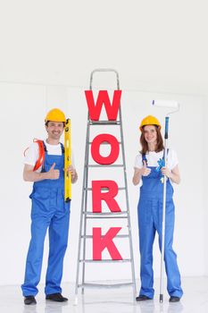 Happy couple in uniform holding tools and ladder with work letters