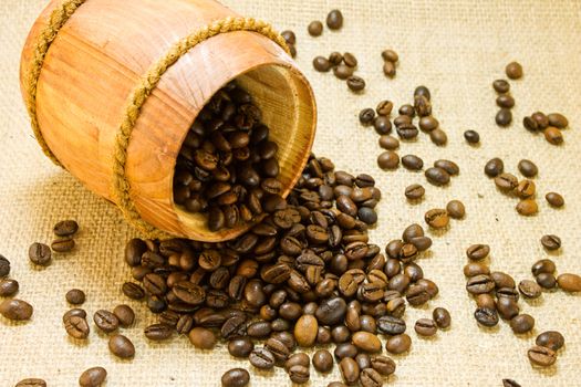 Coffee beans spilled from a lying wooden jar on the background of a sacking