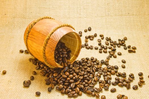 Coffee beans spilled from a lying wooden jar on the background of a sacking