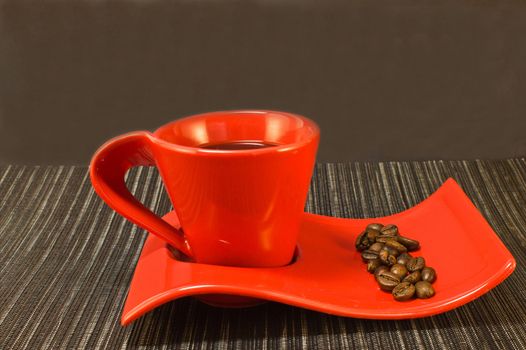 Coffee in red cup and saucer with coffee beans on a black napkin