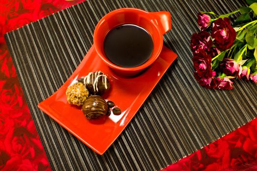 Coffee in red cup on a saucer with a chocolate and a bouquet of roses