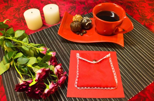 Still life of a coffee in red cup, chocolate, roses, candles and gift envelope