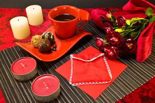 Still life of a coffee in red cup, chocolate, roses, candles and gift envelope