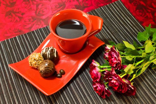 Coffee in red cup on a saucer with a chocolate and a bouquet of roses