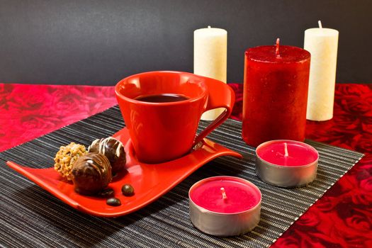 Still life of coffee in a red cup and saucer, and chocolates