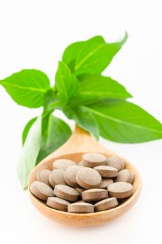 Herbal tablets in wooden spoon with green leaf on white background.