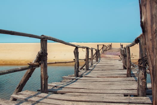 Creative travel photo with blue sky, sea, beach and wood plank road leading far away