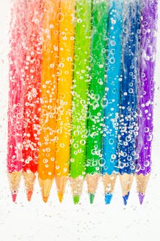 Colorful wooden pencils in soda water with bubbles on white background.