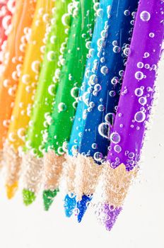 Close up colorful wooden pencils in soda water with bubbles on white background.