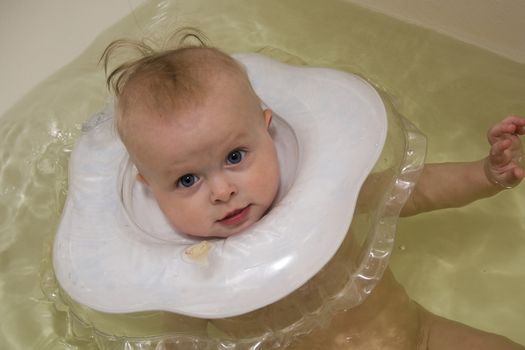 Baby swimming with neck swim ring in bath