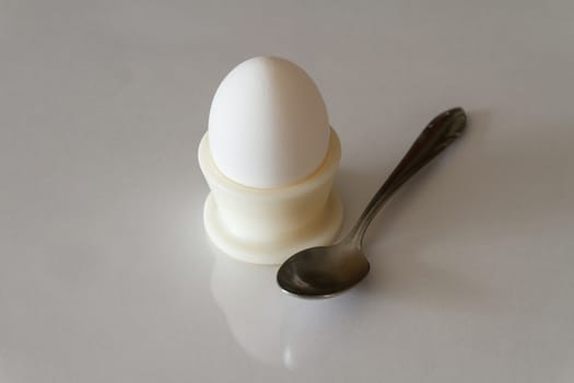Boiled egg in a holder with a spoon on a light background