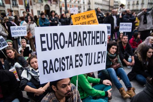 SPAIN, Madrid: A protester holds a sign which reads Euro-Apartheid, racista es tu ley! during a rally at Sol Square in Madrid, Spain on April 22, 2015 to protest against EU-Turkey agreement and to show support to refugees for a 24 hours vigil.