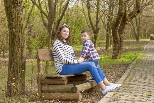 beautiful pregnant woman outdoor with her little boy in the park on bench