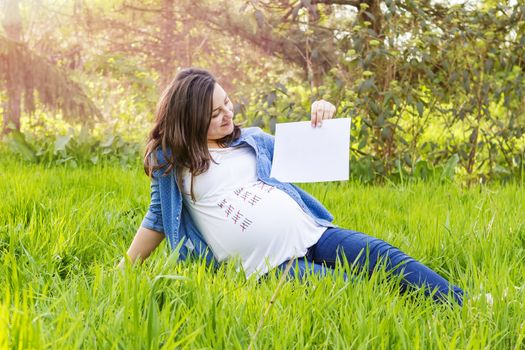 beautiful pregnant woman outdoor with a paper in hand show the day birth of her baby
