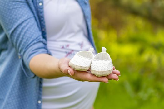 close up of a pregnant woman holding baby shoes in her hands in a park