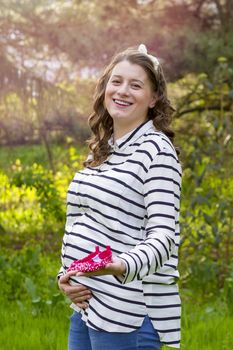 close up of a pregnant woman holding baby shoes in her hands in a park