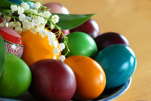various colorful easter eggs on plate with may-lily flower