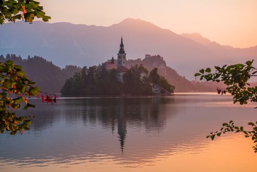 Little Island with Catholic Church in Bled Lake, Slovenia at Sunrise with Castle and Mountains in Background