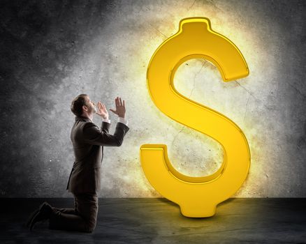 Businessman on knees in front of dollar sign on grey wall background