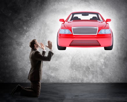 Businessman on knees in front of car on grey wall background