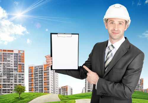 Smiling businessman in helmet showing blank folder on building site