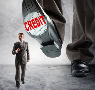Big foot with word credit steps on businessman on grey wall background