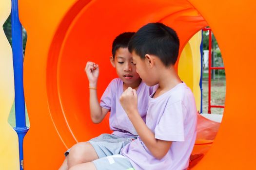 Twin Thai boy playing rock-paper-scissors at playground.