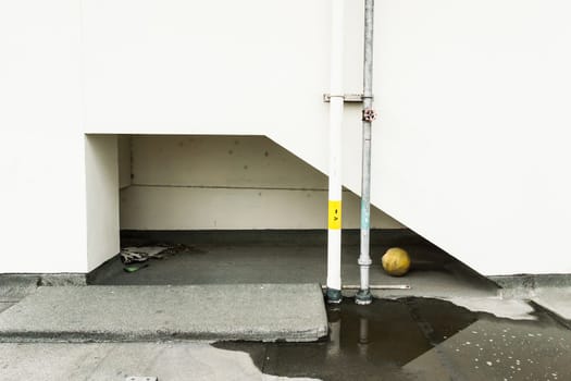 Exterior picture of old white wall,water, ball and water pipe.